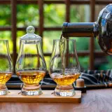 Ein Glas wird mit goldenem Whisky gefüllt, bereit, pur getrunken zu werden. Zwei weitere Gläser stehen daneben.