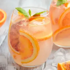 Erfrischender Aperol Lillet mit Blutorangenscheiben und Minze, serviert mit Eiswürfeln auf Holzhintergrund.
