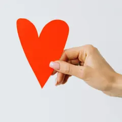 Eine Hand hält ein rotes Herz, das wie eine versteckte Liebesbotschaft wirkt.