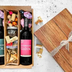 Ein liebevoll zusammengestellter Geschenkkorb zum selber machen: Zwei Flaschen Wein, Pralinen, Kirschmarmelade und Gebäck.