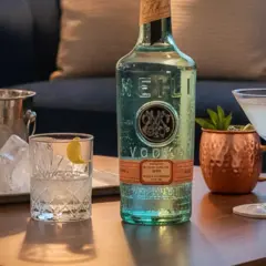 Flasche MEILI VODKA neben Eiswürfeln und Cocktails. Woraus wird Wodka hergestellt? Aus Getreide oder Kartoffeln, destilliert und gefiltert.