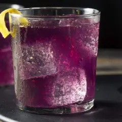 Erfrischender lila Cocktail mit Eis und Zitronenzeste.