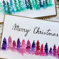 Zwei handgemalte Weihnachtskarten mit Aquarell-Tannenbäumen in Lila- und Grüntönen. Perfekt zum Thema Weihnachtskarten selber malen.