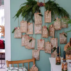 Selbstgemachter Adventskalender für Erwachsene: Kleine Papiertüten mit Hausmotiven und Zahlen hängen an Tannenzweigen.