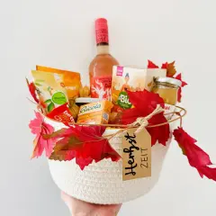 Ein liebevoll gefüllter Geschenkkorb zum Geburtstag, dekoriert mit Herbstlaub. Enthält Wein, Snacks und Honig.