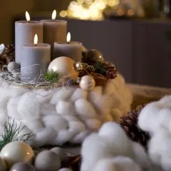 Ein Adventskranz mit vier grauen Kerzen, umwickelt mit dicker, weißer Wolle, dekoriert mit Zapfen und Kugeln.