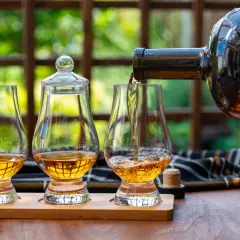 Ein Glas wird mit goldenem Whisky gefüllt, bereit, pur getrunken zu werden. Zwei weitere Gläser stehen daneben.
