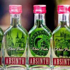 Fünf Flaschen grünen Absinths mit roten Kappen, jede mit einem Etikett, das Prag und die Aufschrift "Absinth" zeigt.