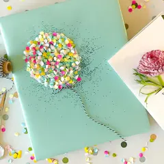 Ein liebevoll gestaltetes Geschenk zum 1. Geburtstag: Geschenkpapier mit Glitzer-Ballon, Schnur, Schere und eine Karte mit Blüte.