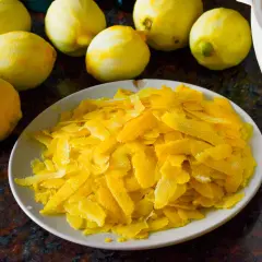 Zitronenschalen liegen auf einem Teller, bereit, um Limoncello herzustellen. Mehrere ganze Zitronen sind im Hintergrund zu sehen.