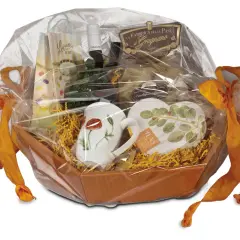 Ein liebevoll zusammengestelltes Geschenk, das mit Folie und orangefarbenen Bändern verpackt ist. Darin befinden sich Tassen, Pasta und weitere Leckereien.