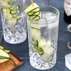 Erfrischender Gin mit Gurke, Eiswürfeln und einer dekorativen Gurkenspirale. Perfekt für einen warmen Sommertag.