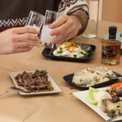 Zwei Gläser mit milchigem Ouzo-Getränk werden angestoßen. Dazu gibt es verschiedene griechische Mezedes und kleine Flaschen Ouzo.