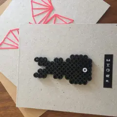 Selbstgemachte Osterkarte: Ein schwarzer Osterhase aus Perlen und ein rotes Muster auf Karton. Frohe Ostern!
