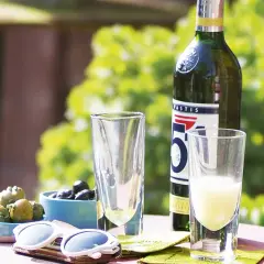 Ein Glas Pastis mit Anis Geschmack, Oliven und Sonnenbrille auf einem Tisch im Freien.