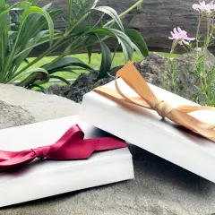Zwei weiße Schachteln, die wie Geschenke aussehen, sind mit roten und goldenen Bändern verziert. Perfekt, um einen Gutschein in Folie zu verpacken.