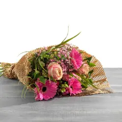 Ein Strauß bunter Blumen, liebevoll als Geschenk verpackt in braunem Papier mit Wabenstruktur, liegt auf einer Holzoberfläche.