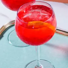 Erfrischender Campari Spritz mit Eis und Orangenscheibe auf einem Tablett.
