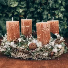 Natürlicher Adventskranz Idee mit vier braunen Kerzen, Moos, Federn und kleinen Glaskugeln auf einem Holztisch.