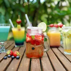 Erfrischende bunte Cocktails mit Früchten und Limette auf einer Holzoberfläche, perfekt für einen Sommertag.