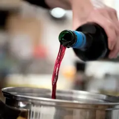 Roter Wein fließt aus einer Flasche in einen Topf. Perfekt als alkohol zum kochen für ein köstliches Gulasch.