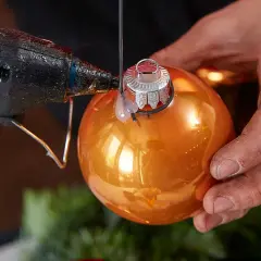 Mit Klebepistole und orangefarbener Kugel einen Adventskranz aus Kugeln selber basteln.