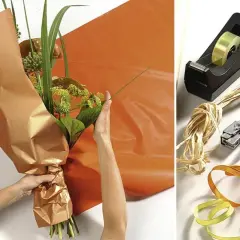 Anleitung: Blumen mit Packpapier verpacken. Hände arrangieren den Strauß, während orangefarbenes Papier bereitliegt. Werkzeuge wie Klebeband, Schere und Bänder sind daneben zu sehen.