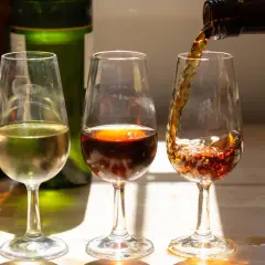 Drei Gläser mit Sherry Aperitif, eines hell, eines dunkelrot, das dritte wird gerade gefüllt.