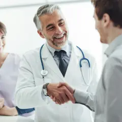 Ein Arzt schüttelt einem Patienten die Hand, ein Lächeln der Zufriedenheit. Im Hintergrund eine lächelnde Krankenschwester. Ein schönes Bild für eine Danksagung Krankenhaus.
