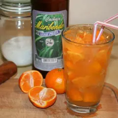 Ein Glas mit Eis und Orangenscheiben, daneben eine Flasche "Cachaça Maribondo". So wird Cachaça, ein brasilianischer Zuckerrohrschnaps, oft serviert.