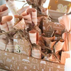 Ein liebevoll gestalteter Adventskalender mit vielen kleinen Päckchen, die mit Häusern und Streifen verziert sind. Tolle Adventskalender Gutscheine Ideen für jeden Tag.