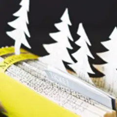 Kreative **Tickets verpacken Ideen**: Ein aufgeschlagenes Buch mit weißen Tannenbäumen und einem Ticket-Einschub, daneben glitzernde Kugeln.