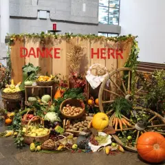 Erntedank: "Danke Herr" steht auf Holz. Reichlich Obst, Gemüse, Brot und Wagenräder schmücken den Tisch.