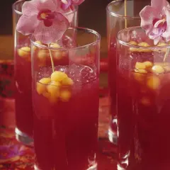Erfrischende asiatische Cocktails mit Melonenbällchen und Orchideen auf einem roten, gemusterten Tuch.