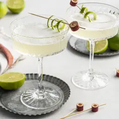 Zwei erfrischende Daiquiri Cocktails mit Limettenschale garniert, umgeben von frischen Limetten.
