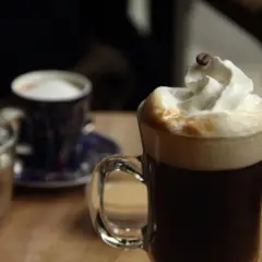 Ein Glas mit Kaffee und Sahne, garniert mit einer Kaffeebohne. Daneben ein kleiner Becher und ein Glas Wasser. Perfekt für einen Kaffee mit Schnaps.