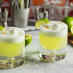 Zwei Pisco Sours mit Limettenspalten und Schaumkrone, bereit für den Genuss.