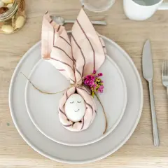 Niedliche Tischdeko Ostern einfach: Ein Ei mit Gesicht, umwickelt von einer Serviette als Hasenohren, mit kleinen Blüten verziert.