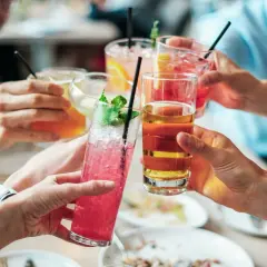 Hände heben bunte Cocktails zum Anstoßen. Eine ausgelassene Cocktailparty mit Freunden.