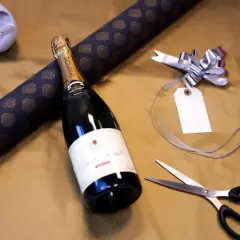 Vorbereitung, um mehrere Flaschen als Geschenk zu verpacken: Champagnerflasche, Geschenkpapier, Schere und Schleife liegen bereit.