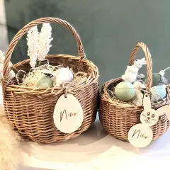 Zwei geflochtene Körbe mit Osterdeko: Eier, Federn, weiße Blumen und Holzanhänger mit Namen. Tolle Osterkorb Ideen für Kinder.
