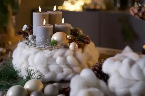 Ein Adventskranz mit vier grauen Kerzen, umwickelt mit dicker, weißer Wolle, dekoriert mit Zapfen und Kugeln.