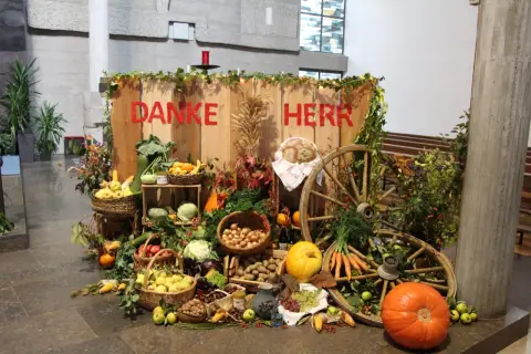 Erntedank: "Danke Herr" steht auf Holz. Reichlich Obst, Gemüse, Brot und Wagenräder schmücken den Tisch.