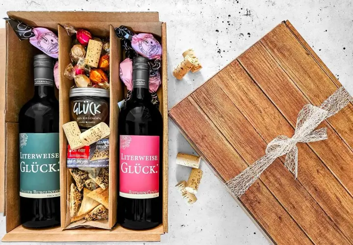 Ein liebevoll zusammengestellter Geschenkkorb zum selber machen: Zwei Flaschen Wein, Pralinen, Kirschmarmelade und Gebäck.