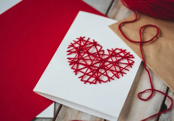 Eine selbstgemachte Valentinstagskarte mit einem roten Herz aus Garn. Perfekt zum Valentinstagskarte basteln.