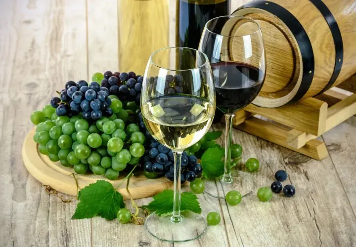 Zwei Gläser Wein, Trauben und ein Holzfass – perfekt für das Kochen mit Alkohol.