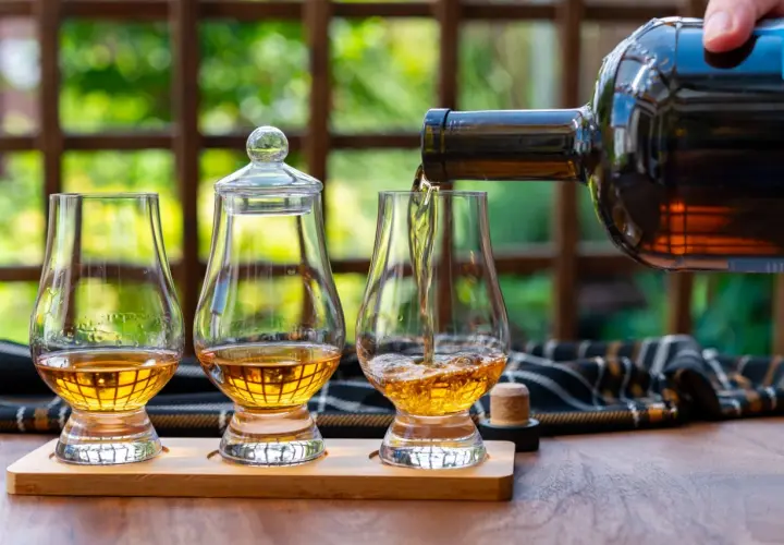 Ein Glas wird mit goldenem Whisky gefüllt, bereit, pur getrunken zu werden. Zwei weitere Gläser stehen daneben.