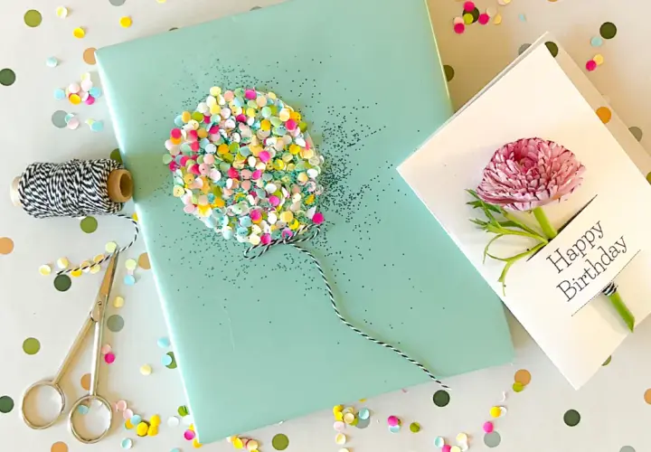 Ein liebevoll gestaltetes Geschenk zum 1. Geburtstag: Geschenkpapier mit Glitzer-Ballon, Schnur, Schere und eine Karte mit Blüte.