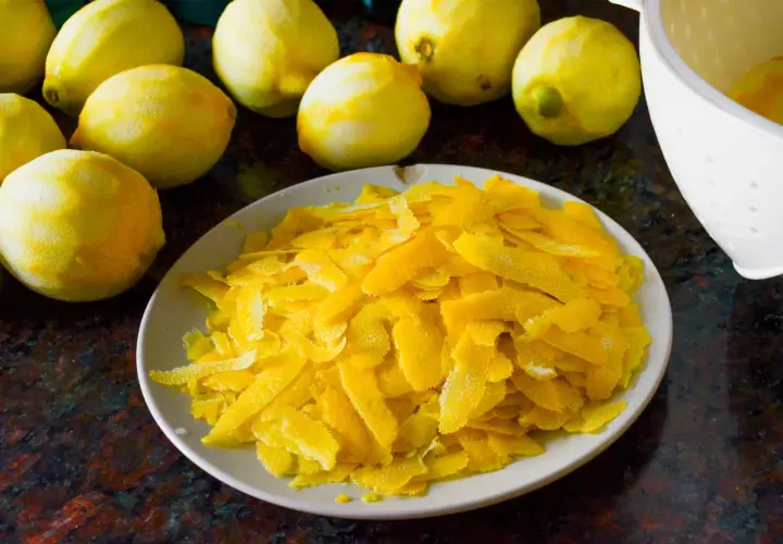 Zitronenschalen liegen auf einem Teller, bereit, um Limoncello herzustellen. Mehrere ganze Zitronen sind im Hintergrund zu sehen.