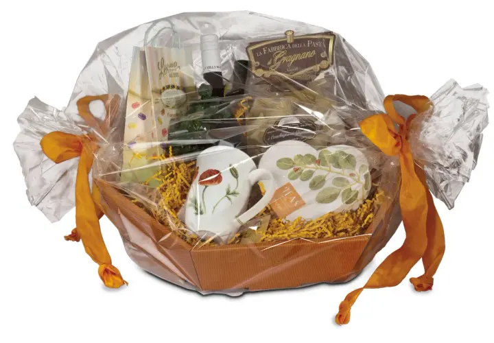 Ein liebevoll zusammengestelltes Geschenk, das mit Folie und orangefarbenen Bändern verpackt ist. Darin befinden sich Tassen, Pasta und weitere Leckereien.